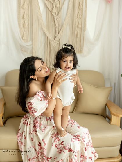 A mother holds her daughter, who is standing on the couch. A playful and sweet moment.