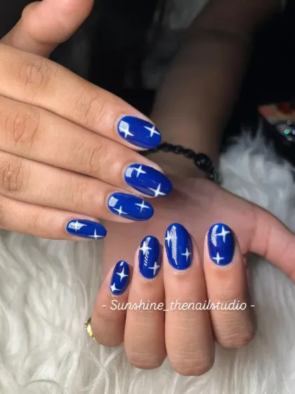 A simple yet striking design. These nails are painted a deep, glossy royal blue and decorated with hand-painted white stars.