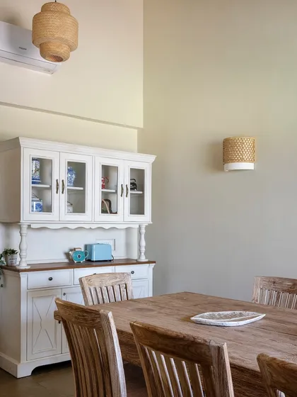 The dining space in the Alibaug villa, where a rustic wooden table is paired with a classic white crockery cabinet. The design is simple, functional, and timeless.