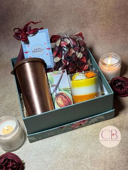 Shine bright with our Diwali delights. This hamper includes a copper tumbler, a layered candle, a bag of potpourri, and a box of chocolates, all packed in a beautiful floral gift box.