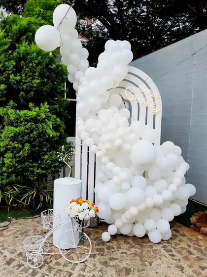 An elegant, all-white balloon installation against a modern arched panel. This minimalist and chic design is versatile for any celebration, from bridal showers to birthdays, and is accented with a small pop of color from the flowers.