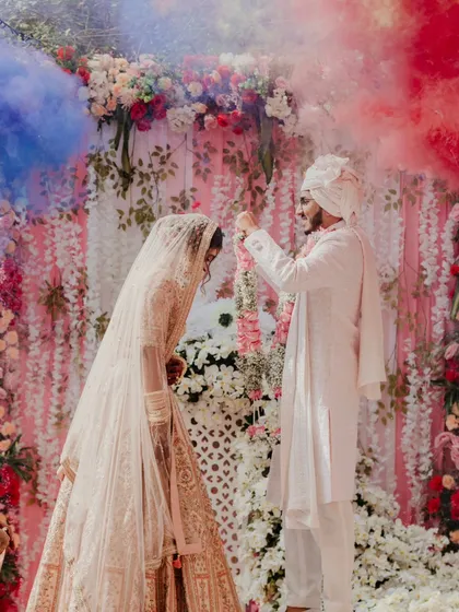A dramatic varmala moment with colored smoke, creating a vibrant and energetic frame. This shows how I can add a touch of Bollywood drama to your wedding photos.