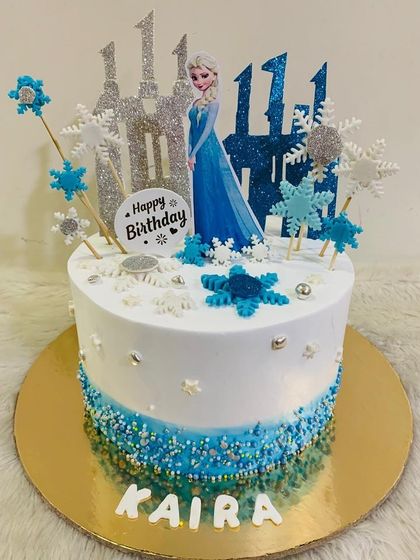 A sparkling Frozen cake for an 11th birthday. This design features Queen Elsa in front of a glittery ice castle, surrounded by delicate snowflakes and blue sprinkles.