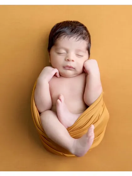 A perfect example of the classic "tucked-in" pose. Wrapped snugly in a mustard swaddle, this portrait highlights the baby's peaceful face and tiny feet.