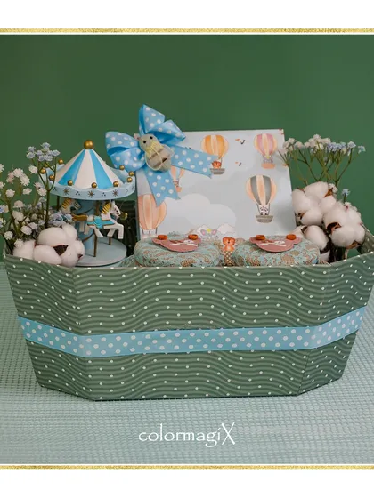 A classic baby boy hamper featuring a charming hot air balloon theme. This gift set includes a musical carousel and other keepsakes, all presented in a stylish green and blue boat-shaped basket, perfect for a newborn celebration.