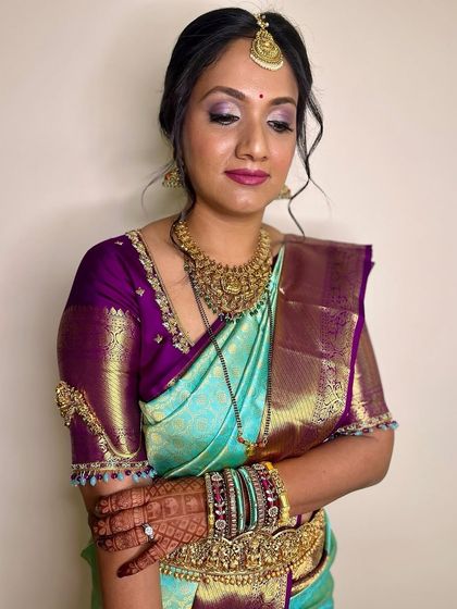 This bride's reception look is a beautiful blend of tradition and modernity. The makeup features a soft smokey eye and a berry lip, complementing her turquoise and purple saree.