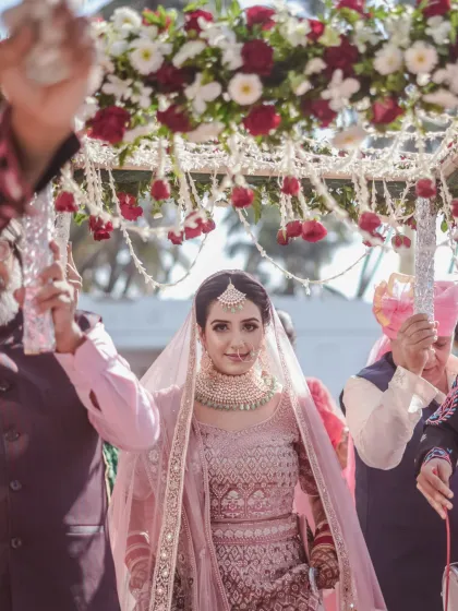The bride's grand entrance under a beautiful 'phoolon ki chadar'. Her direct gaze at the camera captures her confidence and anticipation in this iconic wedding moment.
