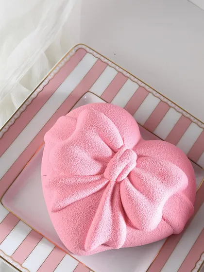 A heart-shaped mousse cake with a beautiful pink velvet texture, shaped like a bow. It's as elegant as it is delicious.
