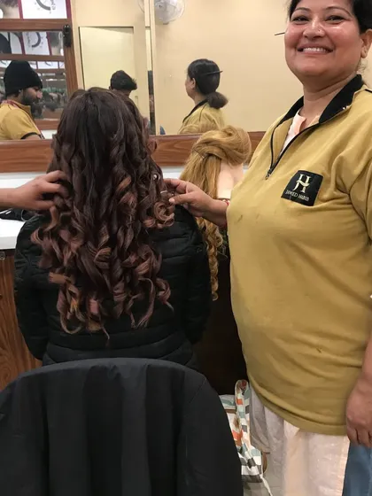 A student proudly stands by her work, a beautifully executed curly hairstyle on a client. This image captures the satisfaction and confidence gained through our practical training.