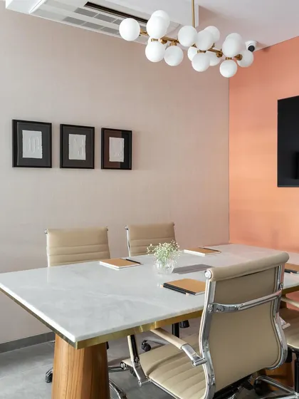 The conference room combines a marble-topped table with comfortable leather chairs and a modern bubble chandelier. The peach-colored accent wall adds a touch of warmth and personality to the space.