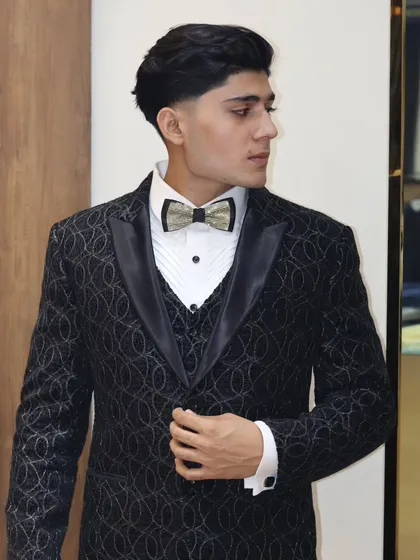 The full view of the black textured tuxedo, showing the satin lapels and the way the fabric catches the light. A perfect choice for a wedding reception.