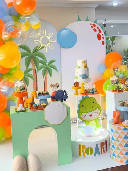 ROAR! Our dinosaur theme parties are a blast of color and fun. This setup shows a complete dessert station with a custom 'ROAR' light-up sign, adorable dino cutouts, and a vibrant balloon garland, perfect for a prehistoric adventure.