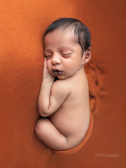 A precious one-week-old newborn, curled up and sleeping on a warm orange backdrop. The simplicity of the pose highlights their tiny, perfect form.