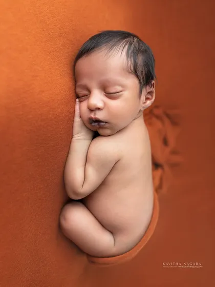 A precious one-week-old newborn, curled up and sleeping on a warm orange backdrop. The simplicity of the pose highlights their tiny, perfect form.