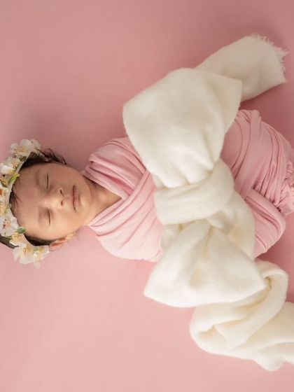 A newborn wrapped in pink fabric with a white bow, posed diagonally for a dynamic and sweet composition.