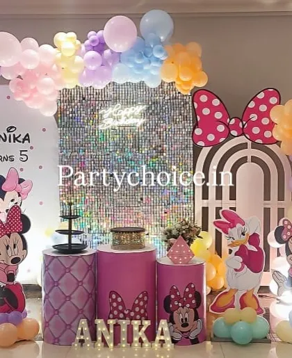 A pastel Minnie Mouse theme perfect for a magical birthday. This setup features a shimmering silver sequin backdrop, a multi-colored pastel balloon arch, and life-sized cutouts of Minnie, Daisy, and Pluto, all personalized with the birthday girl's name in light-up letters.
