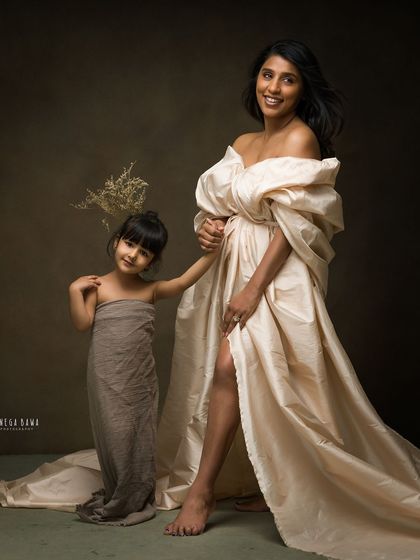 A full-length fine art portrait of a mother and daughter. The elegant gown and dramatic lighting create a sense of timeless grace.