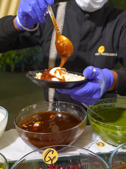 A chef carefully assembling a plate of Dahi Bhalla, drizzling sweet tamarind chutney over the yogurt-soaked lentil dumplings.