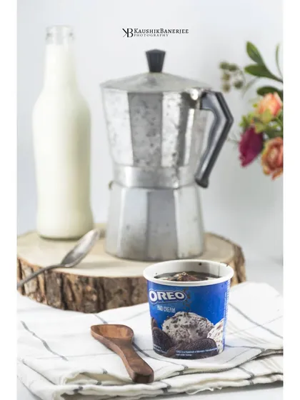 A tub of Oreo ice cream styled with a vintage coffee pot and milk bottle. This setup creates a nostalgic, comforting feel for a product shoot, making the ice cream feel like a special treat.