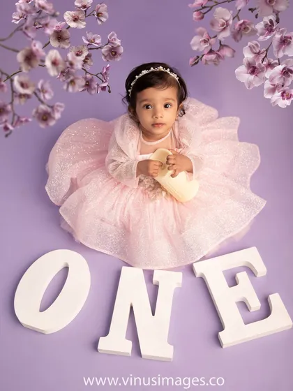 One year of wonder. This sweet first birthday portrait shows the baby girl in a fluffy pink dress, surrounded by cherry blossoms and the word "ONE".