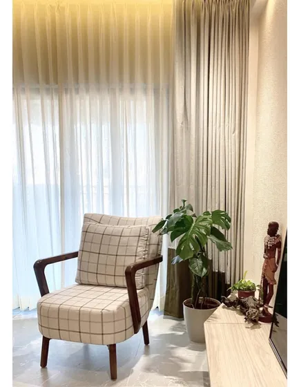 This cozy corner features a classic armchair with a modern checked pattern, perfect for reading. The layered curtains and indoor plant add to the warm, earthy feel of the room.