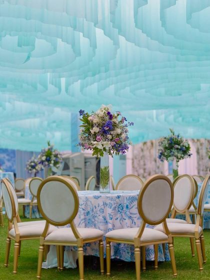 Elegant table setting at the Dior-themed Mehendi. The tables are dressed in custom-printed linens matching the backdrop, topped with beautiful floral centerpieces in shades of blue, purple, and white.