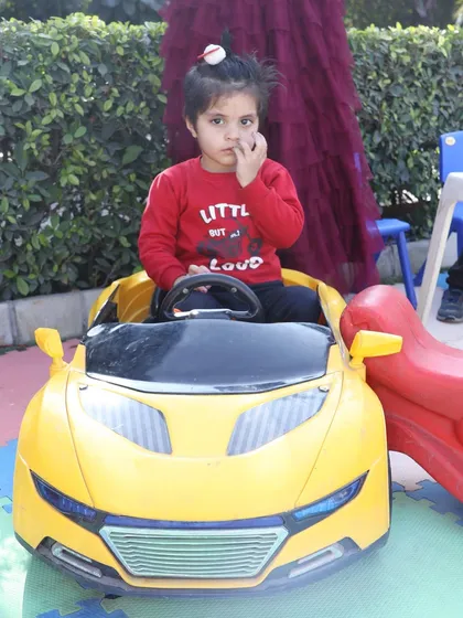 A young girl posing in a bright yellow toy car. These ride-ons are perfect for photo opportunities and make for a grand entrance at a first birthday party.