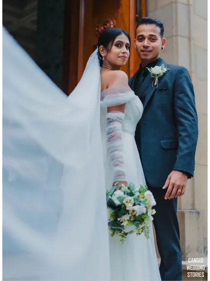 A classic wedding portrait with a touch of drama. The bride's veil flowing in the wind adds a beautiful, dynamic element to this elegant shot outside the church.