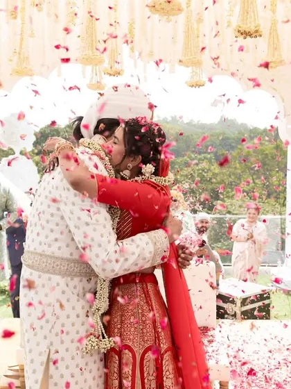 A moment of pure joy for the couple, framed by the elegant white mandap and a shower of fresh flower petals.