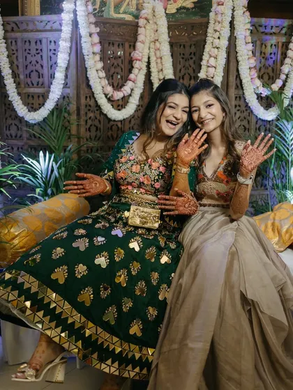 Happy faces and beautiful henna, this is what a successful Mehendi party looks like. The decor, featuring a traditional carved panel and lush floral garlands, creates a festive and celebratory mood.