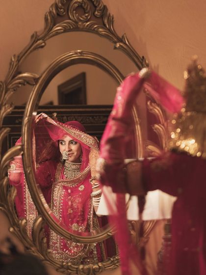 A moment of reflection. The bride, in her delicate veil and rani pink outfit, looks timeless in this vintage-style mirror.