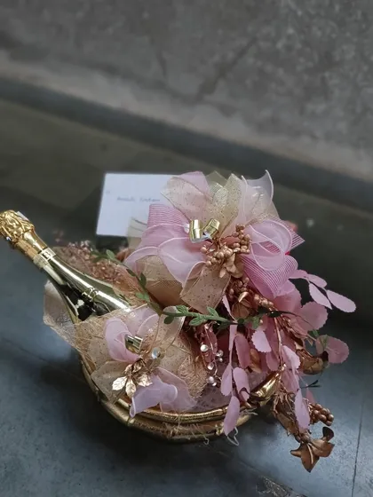 A miniature champagne bottle transformed into a beautiful gift with elaborate pink and gold wrapping. This is a perfect example of how we can make even a small gesture feel grand.