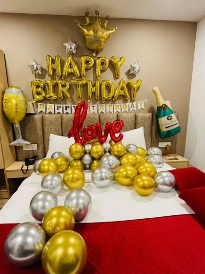 A fun and celebratory birthday decoration with a royal touch. This setup includes gold and silver chrome balloons, 'Happy Birthday' foil letters, and playful additions like a crown, champagne bottle, and wine glass foil balloons.