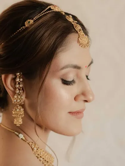 The side profile highlights the intricate bridal bun with fresh flowers and the soft, glowing finish of the skin. Every detail is intentional.