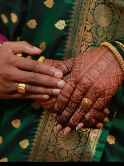 A close-up of the couple's hands, showing the intricate back-hand mehndi design. The dark stain looks beautiful against her traditional green saree.