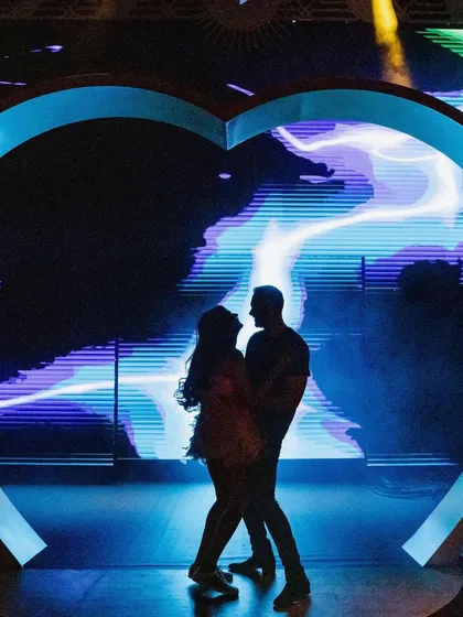 A silhouette of Vanshika and Aneesh against a massive LED screen, with the Dubai Eye in the background. This modern, graphic portrait is uniquely Dubai.