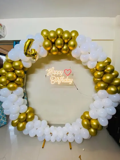 An elegant gold and white circular balloon arch for a 4th birthday party, complete with a 'Happy Birthday' neon sign.