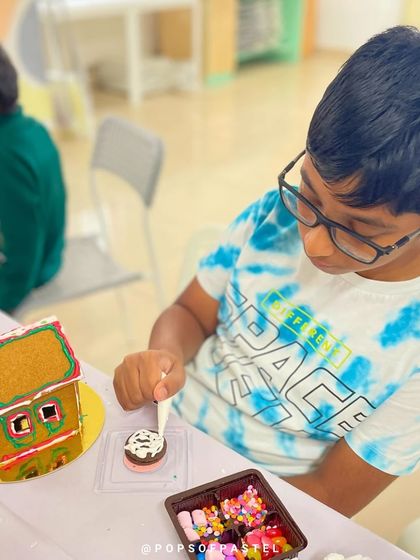 A young boy adds the final touches to his gingerbread house, carefully placing candies on the roof.