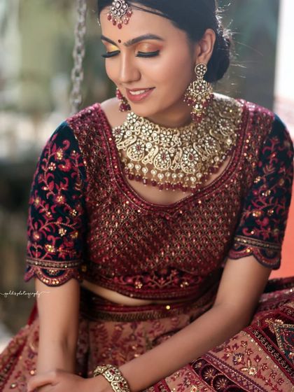 A close-up shot focusing on the bride's happy expression and the magnificent statement necklace. The soft lighting enhances the sparkle of the jewelry and the richness of the fabric.