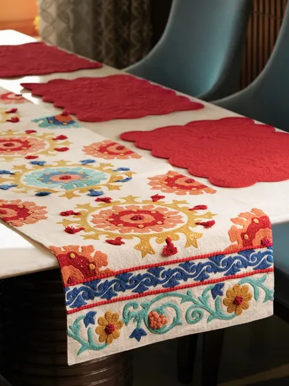 A vibrant, multi-colored embroidered table runner paired with bright red placemats. This colorful tablescape is full of energy and showcases how different textiles can be layered for a festive look.