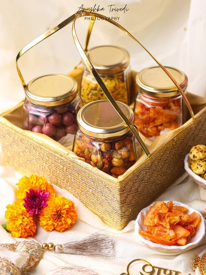 A hamper basket filled with jars of pickles and snacks. The styling with marigold flowers and traditional tassels makes it perfect for festive Indian gifting.