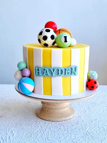 A full view of the striped, ball-themed cake on its stand.