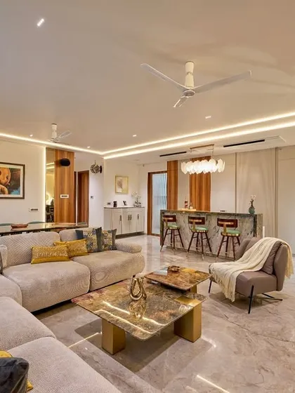 This open-plan residence showcases our expertise in creating harmonious living and dining spaces. We designed this area with a plush sectional sofa for comfort, a custom marble-top coffee table, and a stylish bar counter, all unified by sophisticated layered lighting to create an atmosphere of warm, inviting luxury.