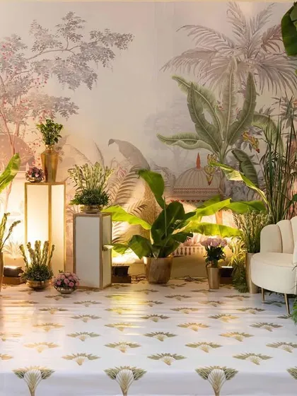A beautiful stage setup for a 'Shrimant' (baby shower) ceremony. The design features a custom botanical wallpaper, lush banana trees, and elegant seating, creating a serene and traditional garden atmosphere.