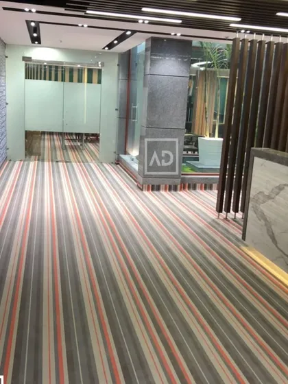 For this modern office lobby, I used striped wall-to-wall carpet to create a sense of direction and space. This type of commercial carpeting is designed for high foot traffic and provides sound insulation, which is essential in a busy work environment.