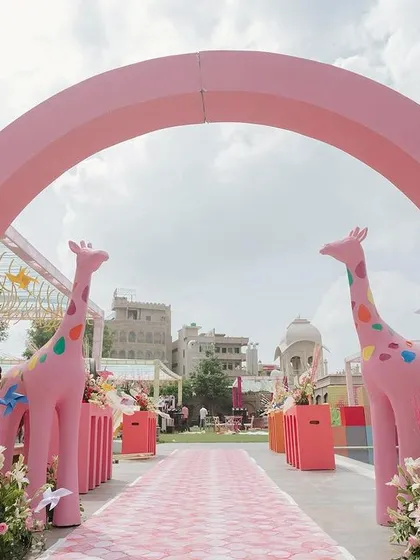 The grand entrance to the carnival Mehendi, marked by a large pink arch and flanked by two playful giraffe statues, setting a fun and festive tone.