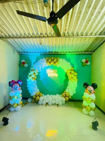A wider view of the Mickey and Minnie Mouse birthday setup, showing the full circular balloon backdrop against a green wall.