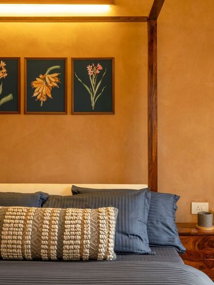 A close-up of the bedroom, highlighting the textural interplay between the woven cushions, striped linens, and the smooth, rustic finish of the wall. The botanical art prints above the bed further enhance the natural theme.