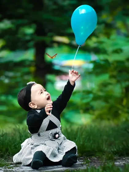 A moment of pure joy during a candid baby photoshoot. I love capturing these unscripted interactions, like this little one reaching for a balloon, with the soft, natural light creating a dreamy outdoor portrait.
