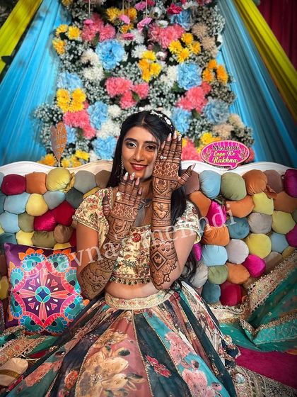 A happy bride in a colorful setting, showing off her beautiful mehndi. The design is a mix of modern and traditional, with geometric patterns and floral details that complement her vibrant outfit.